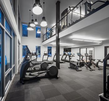 A gym with cardio machines and weights in a building with a staircase